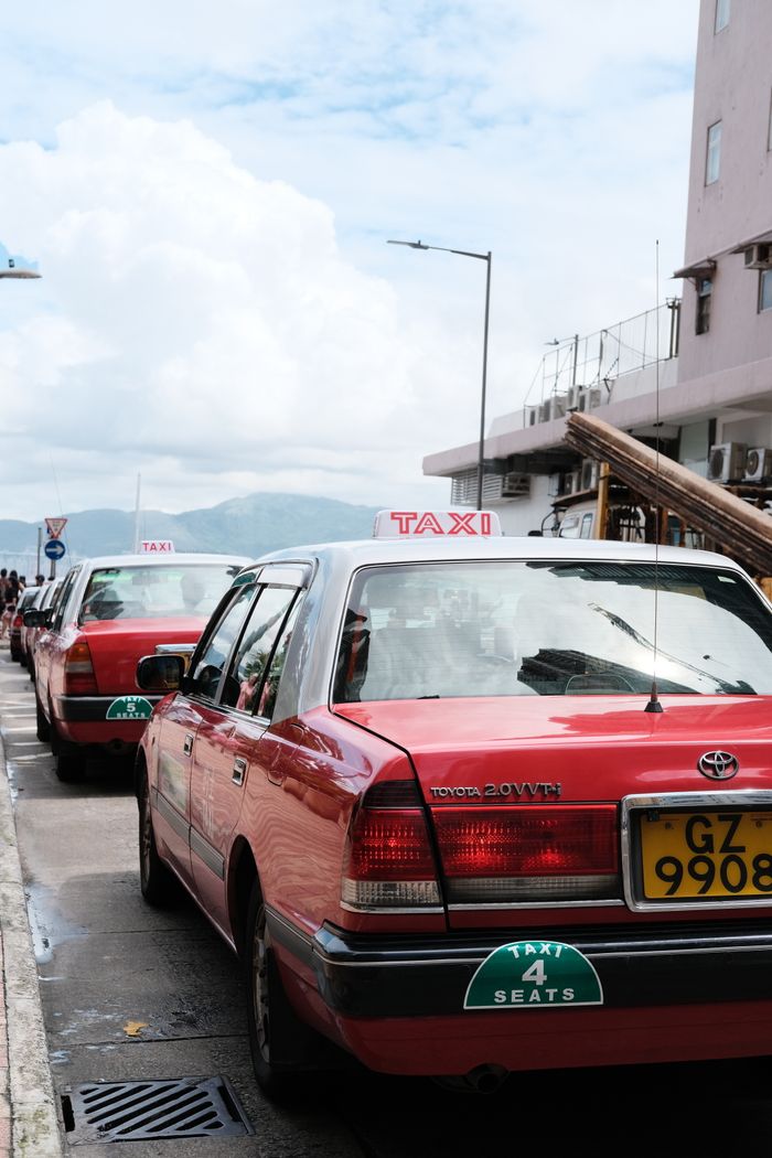 Red taxis parked along a street in a city with a clear sunny sky, ready for passengers.